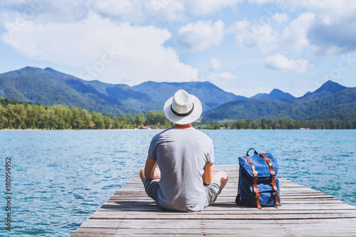 summer travel, young romantic man tourist wanderlust sitting on wooden pier photo