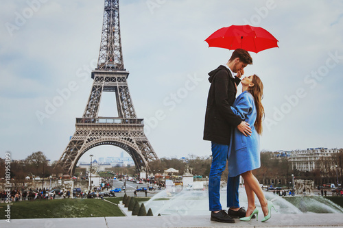 romantic affectionate couple kissing under  umbrella near Eiffel Tower, honeymoon in Paris