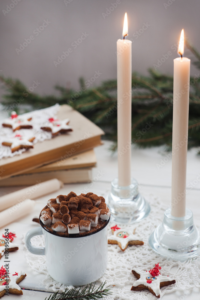 Christmas and new year holiday celebration concept background. Cup of cocoa with marshmallow, homemade cookie, lighted candles, xmas tree decoration on wooden table.
