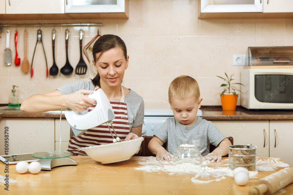 Little kid boy helps mother to cook Christmas ginger biscuit in light kitchen with tablet on the table. Happy family mom 30-35 years and child 2-3 in weekend morning at home. Relationship concept Little kid boy helps mother to cook Christmas ginger biscuit in light kitchen with tablet on the table. Happy family mom 30-35 years and child 2-3 in weekend morning at home. Relationship concept