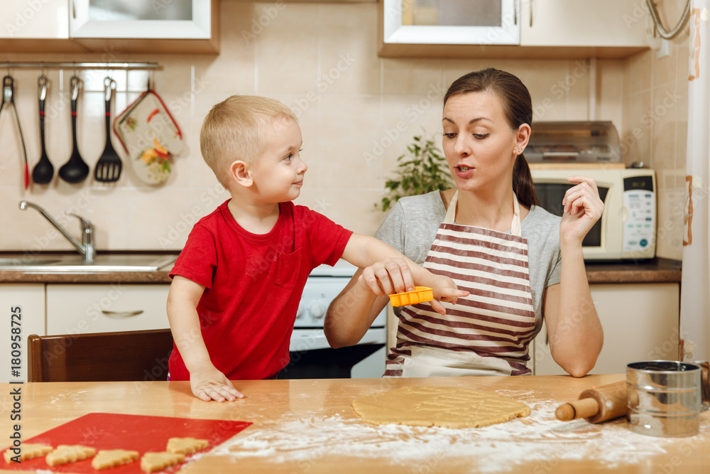 Little kid boy helps mother to cook Christmas ginger biscuit in light kitchen. Happy family mom 30-35 years and child 2-3 roll out dough and cut out cookies at home. Relationship and love concept Little kid boy helps mother to cook Christmas ginger biscuit in light kitchen. Happy family mom 30-35 years and child 2-3 roll out dough and cut out cookies at home. Relationship and love concept