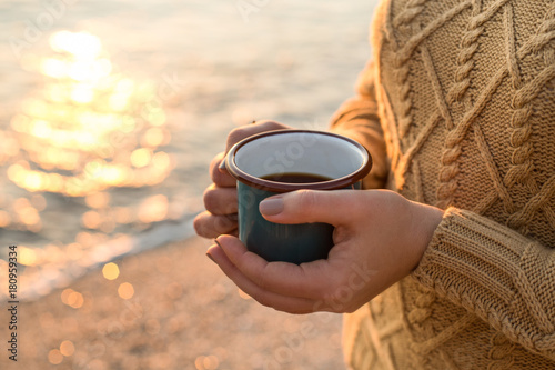 Cozy autumn by the sea. Female hands holding a mug with tea