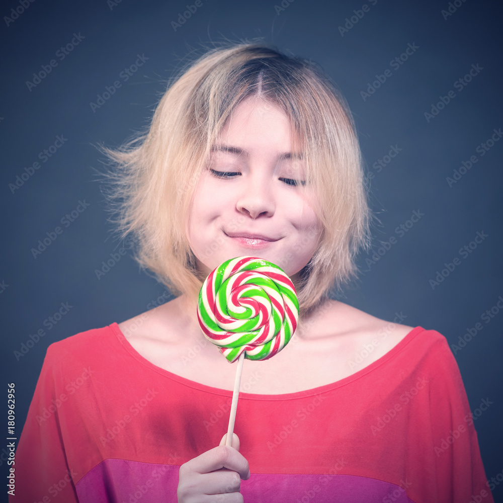 blonde girl teenager in a red blouse looking at the lollipop  on a gray background. Toned