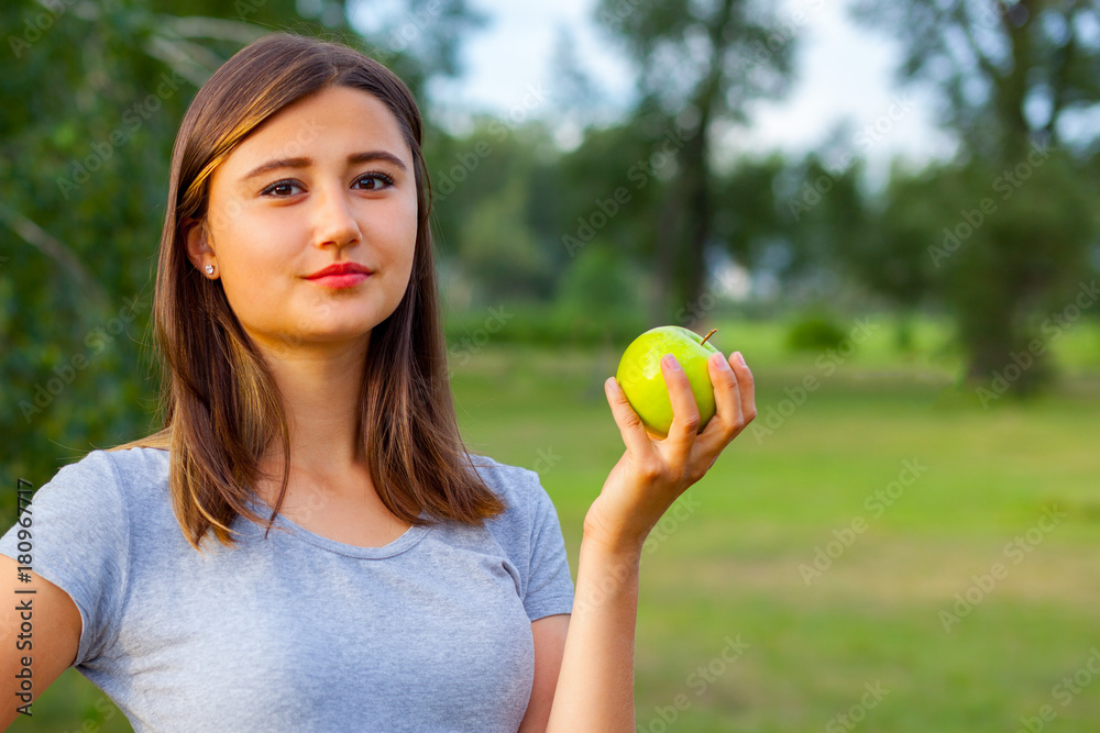 Beautiful teenage girl biting an apple, against green of summer park. Beautiful teenage girl biting an apple, against green of summer park.