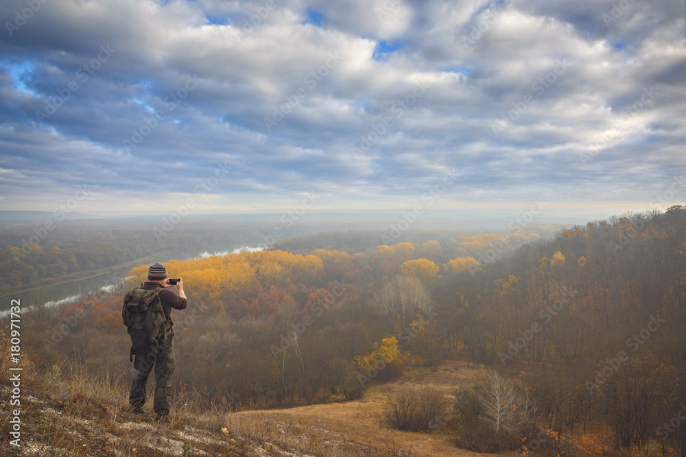 A tourist with a backpack photographed the autumn landscape.