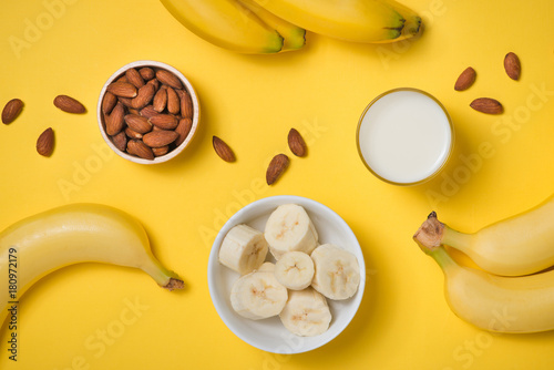 Almond milk in a glass with almond nuts and bananas on a yellow background. Healthy food and drink concept.