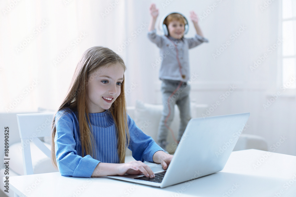 Different activities. Active energetic boy jumping while his sister working on a laptop Different activities. Active energetic boy jumping while his sister working on a laptop