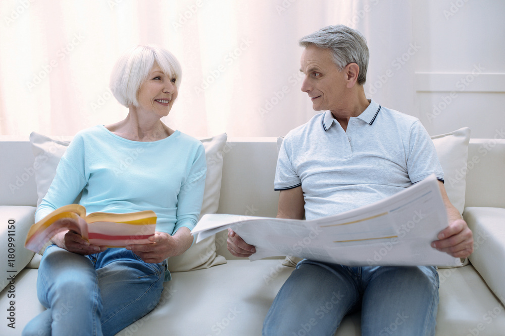 Obraz premium Nice readers. Cheerful friendly old people sitting on a comfortable sofa together and reading