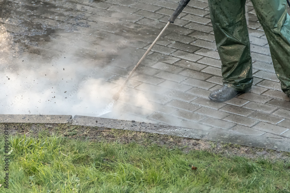 Obraz premium Worker cleaning driveway with high pressure water jet, high pressure cleaner. High pressure deep cleaning.