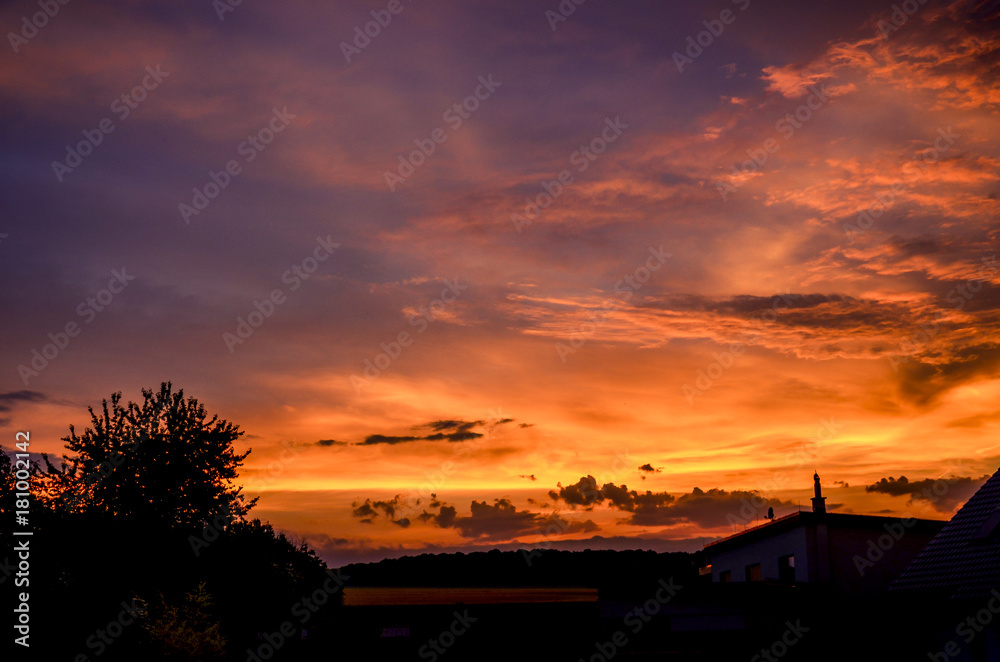 Bright red sunset over silhouetted houses.