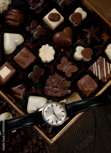 Box of chocolate pralines and on top of it a luxury watch prepared for a gift