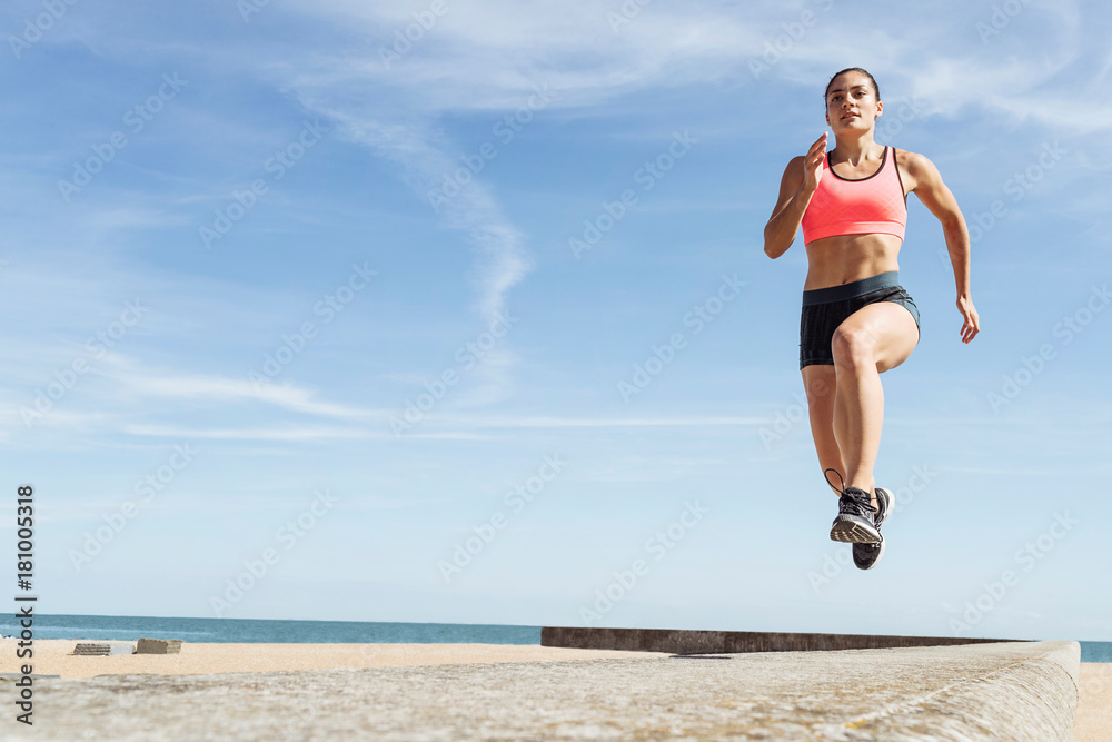 Young woman running along sea wall, mid air Young woman running along sea wall, mid air