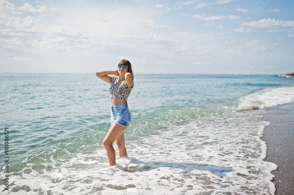 Beautiful model relaxing on a beach of sea, wearing on jeans short, leopard shirt and sunglasses. Beautiful model relaxing on a beach of sea, wearing on jeans short, leopard shirt and sunglasses.