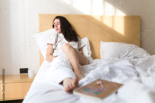 Brunette girl, young women on bed with cup of coffee and notebook. Lazy morning in hotel