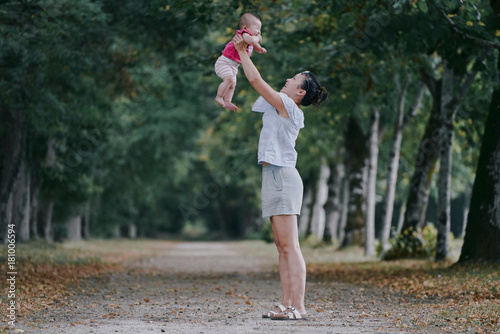 Woman holding up baby daughter in tree lined park, Chenonceaux, Loire Valley, France