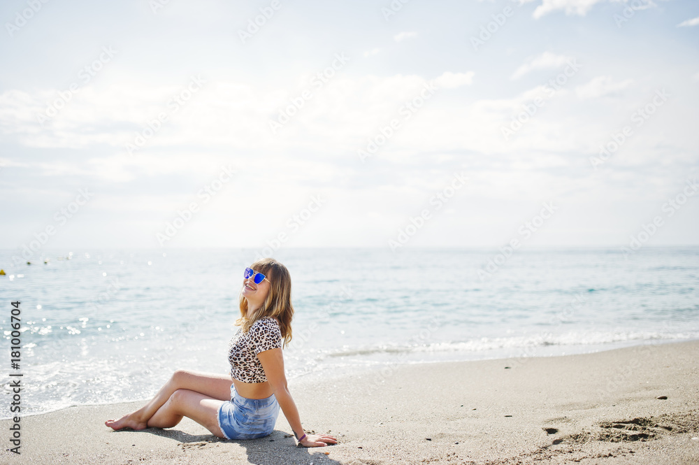 Beautiful model relaxing on a beach of sea, wearing on jeans short, leopard shirt and sunglasses. Beautiful model relaxing on a beach of sea, wearing on jeans short, leopard shirt and sunglasses.