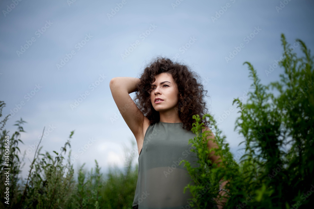 portrait of curly brunette in field on sky background portrait of curly brunette in field on sky background