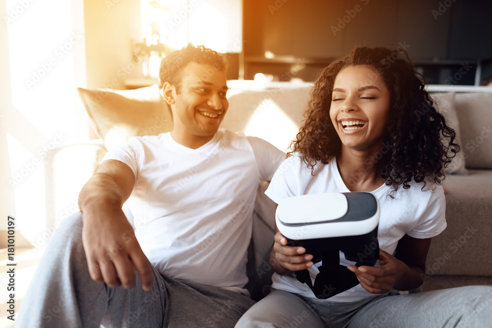 Black man and woman are sitting on the couch. A man and a woman hold a helmet of vr in their hands and dispose of it. Black man and woman are sitting on the couch. A man and a woman hold a helmet of vr in their hands and dispose of it.