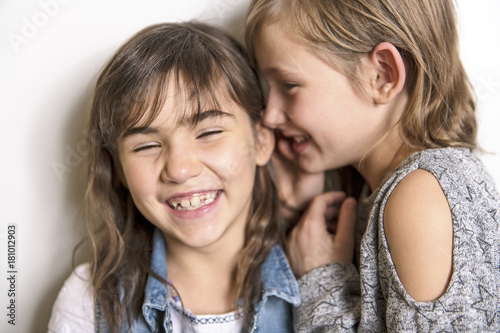 Two happy kids sister standing at blank grey wall and embracing