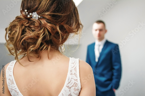 Bride standing with her back to the camera looking at the groom in the defocus