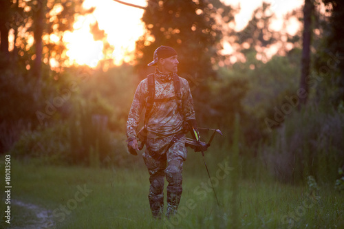 Mature man walking in rural setting, carrying crossbow