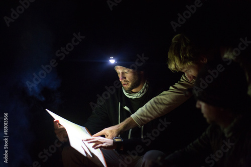 Three men looking at map, at night, using headlamp for light