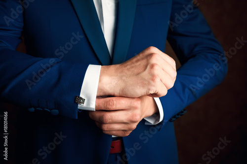 A man in a blue suit straightens his sleeves