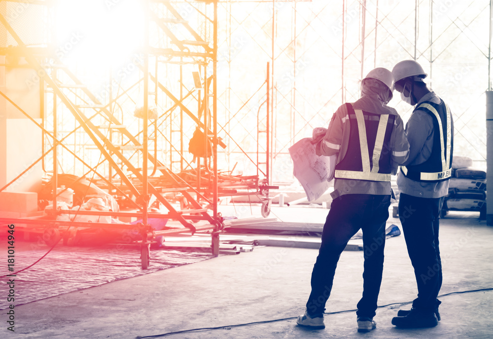 Fototapeta premium Silhouette engineer in safety protective equipment standing orders for construction crews to work at building construction site. It's a key successfully for business, successful concept