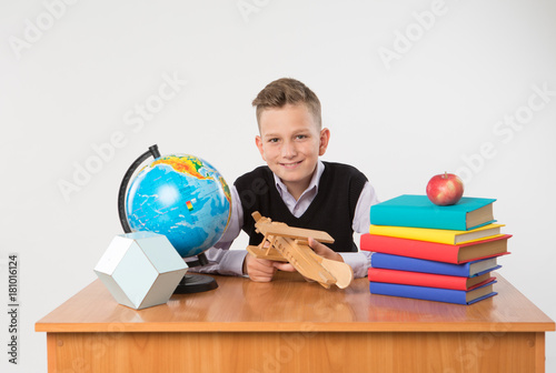 Cute happy schoolboy sit at a school desk isolated on white background. Ideal for banners, registration forms, presentation.
