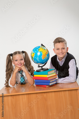 Happy boy and girl sit at a school desk, isolated on white background. Ideal for banners, registration forms, presentation, landings, presenting concept.