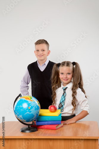 Happy boy and girl standing at a school desk, isolated on white background. Ideal for banners, registration forms, presentation, landings, presenting concept, school concept.