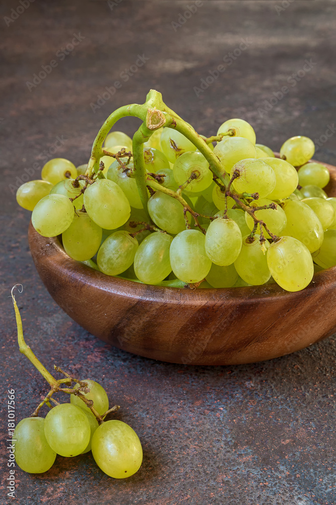 Branch of a green grapes on a wooden plate on a dark background with copy space and selective focus Branch of a green grapes on a wooden plate on a dark background with copy space and selective focus