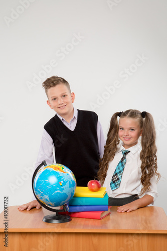 Happy boy and girl standing at a school desk, isolated on white background. Ideal for banners, registration forms, presentation, landings, presenting concept, school concept.