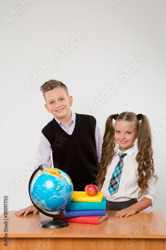 Happy boy and girl standing at a school desk, isolated on white background. Ideal for banners, registration forms, presentation, landings, presenting concept, school concept.