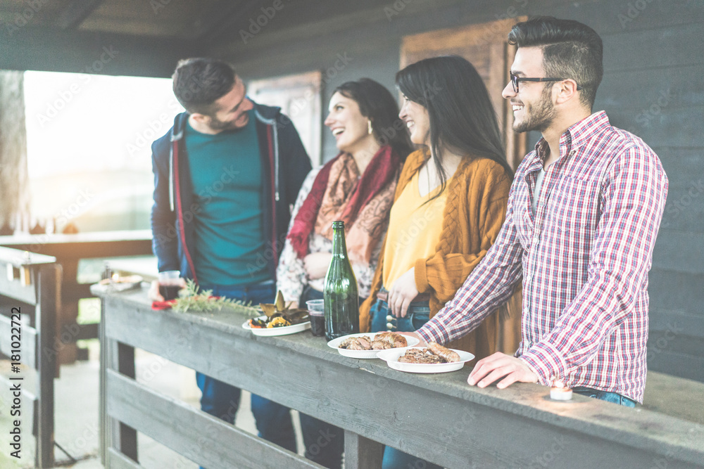Happy friends drinking red wine and eating barbecue outside of mountain wooden house - Young people having fun at bbq party - Youth concept - Focus on right man face - Contrast sunset filter