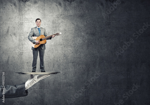 Businessman on metal tray playing acoustic guitar against concrete wall background © adam121