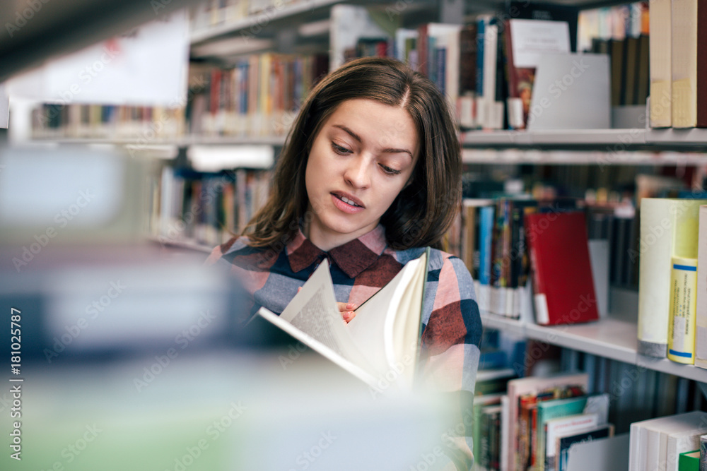 Young female girl student smiling with book in library
Young female girl student smiling with book in library