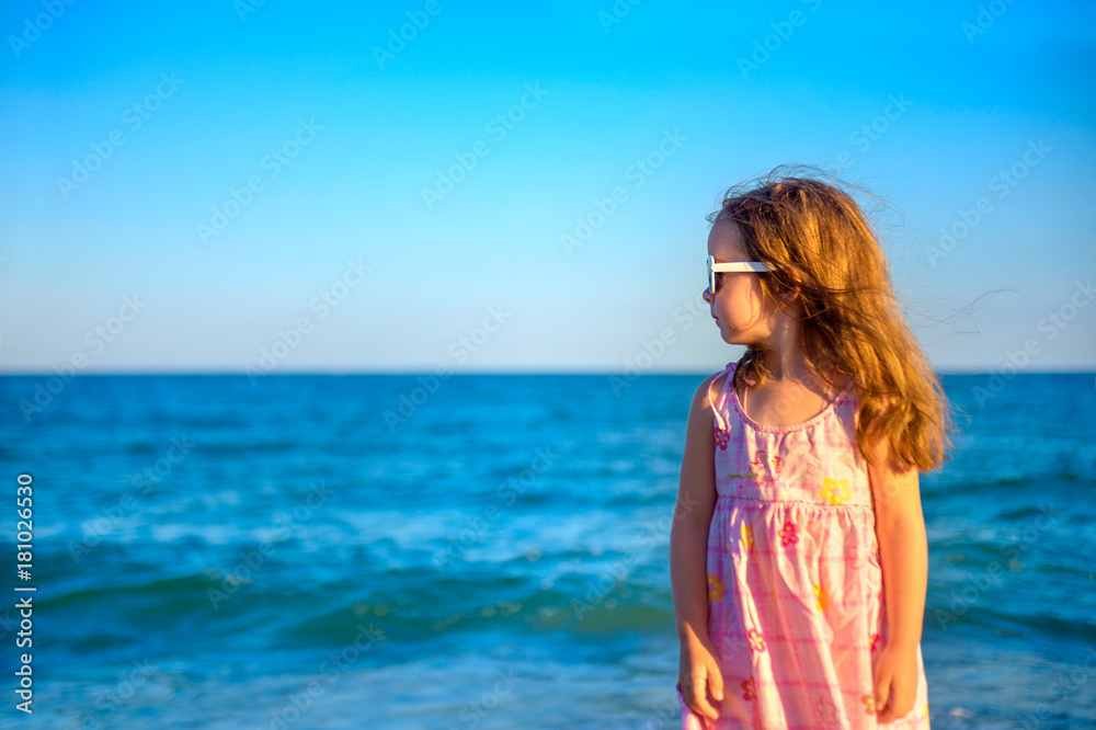 little beautiful girl in a dress standing on the beach looking away and dreaming of something. little beautiful girl in a dress standing on the beach looking away and dreaming of something.