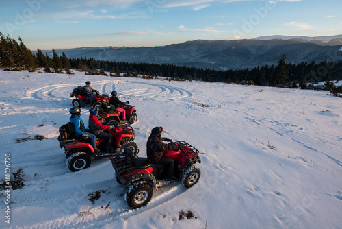 Group of people sitting on off-road four-wheelers ATV bikes in the the mountains in winter evening