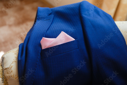 Expensive men's blue jacket lying on the couch with a pink handkerchief in his pocket. Closeup photo