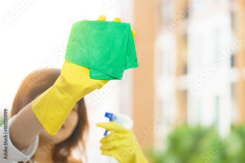 Woman housekeeper cleaning the mirror with green cloth.