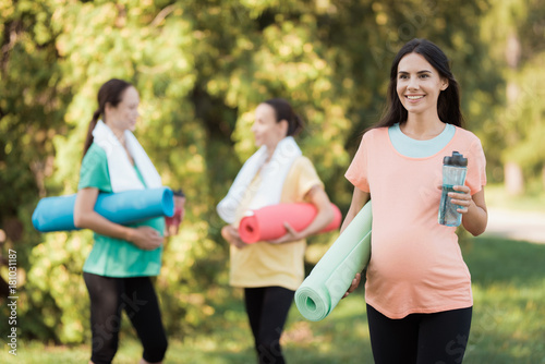 Three pregnant girls came to the park on fitness. A girl in a pink t-shirt posing in the foreground