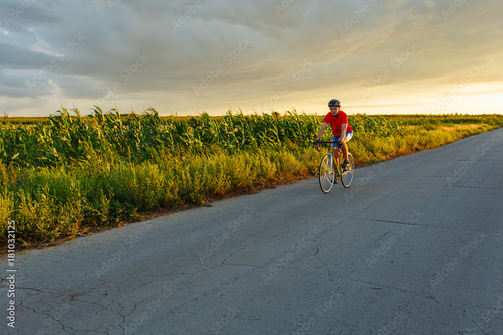 Obraz premium A cyclist rides on a road bicycle along field. In the background sunset sky.