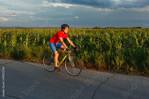 A cyclist rides on a road bicycle along field. In background a beautiful blue sky.