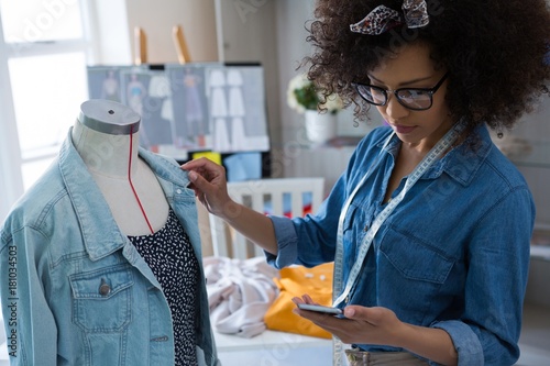 Female fashion designer using mobile phone while designing dress