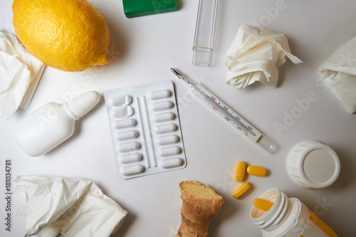 The concept of the common cold. used crumpled napkins, nasal drops, blister with tablets, jar with yellow tablets, thermometer, lemon and ginger root. 