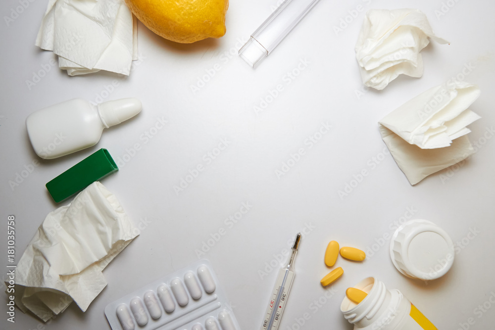 The concept of the common cold. used crumpled napkins, nasal drops, a blister with pills, a jar with yellow pills, a thermometer, a lemon and a ginger root. A frame of objects in the center white The concept of the common cold. used crumpled napkins, nasal drops, a blister with pills, a jar with yellow pills, a thermometer, a lemon and a ginger root. A frame of objects in the center white