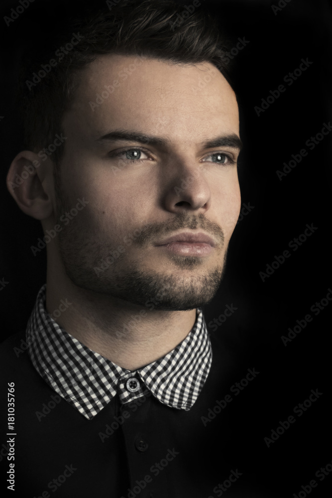 Foto de Dark portrait of fashion male model with green eyes and sharp lined  face and serious looking out of camera on black background. Portrait photo  of successful man (male model) with