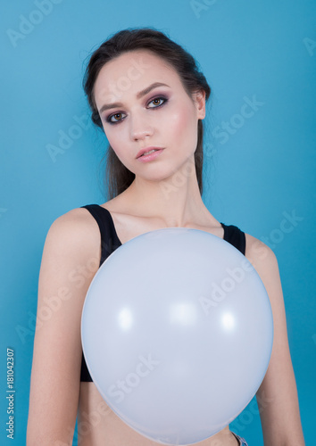 Brunette girl in a black top, holding white balloon on a blue background