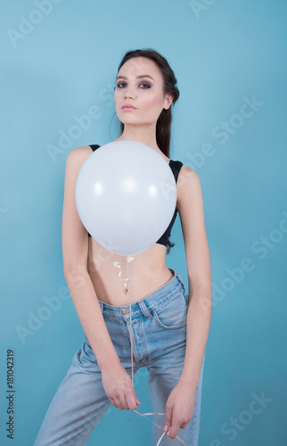 Brunette girl in jeans and a black top, holding white balloon on a blue background